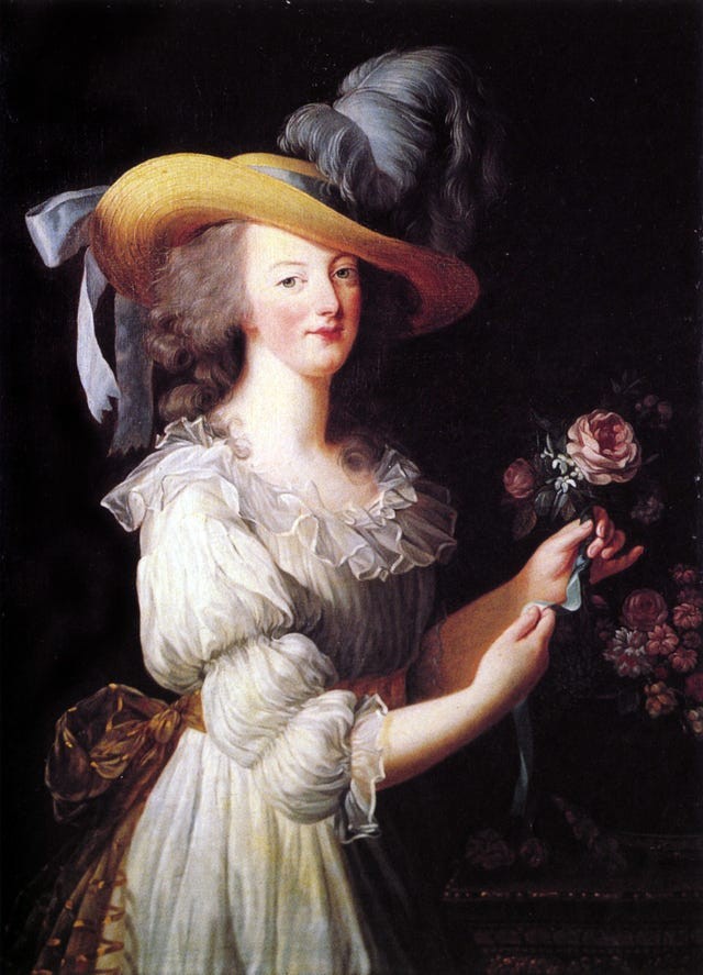 Woman in a white dress and yellow hat holding a flower with a dark background.
