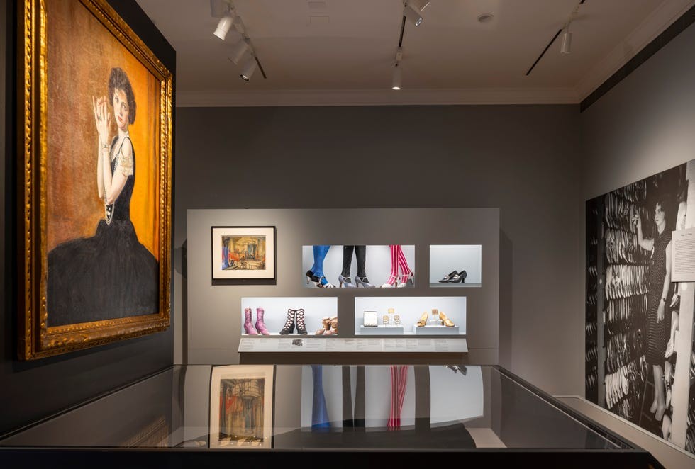 Art exhibit featuring paintings and displayed footwear in a stylish gallery setting.