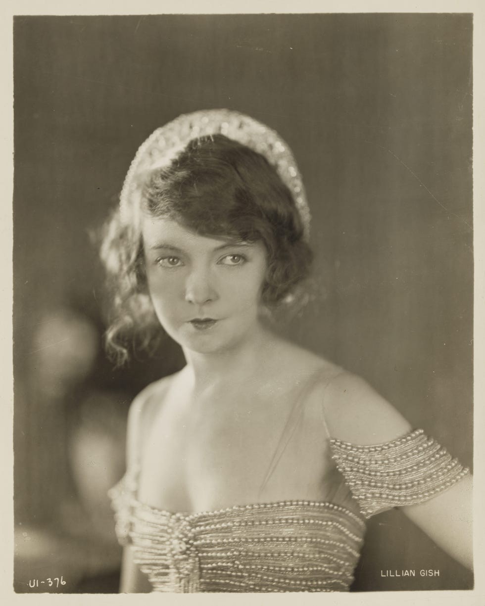 A portrait of a woman with curly hair wearing an embellished dress, gazing thoughtfully at the camera.