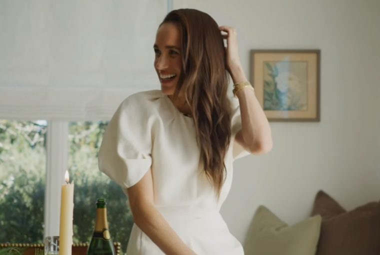 A woman with long hair smiles while adjusting her hair at a beautifully set table with candles and champagne.