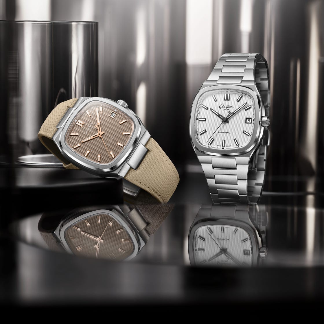 Two elegant watches, one with a beige strap and brown face, the other with a silver bracelet and white face, reflecting on a surface.