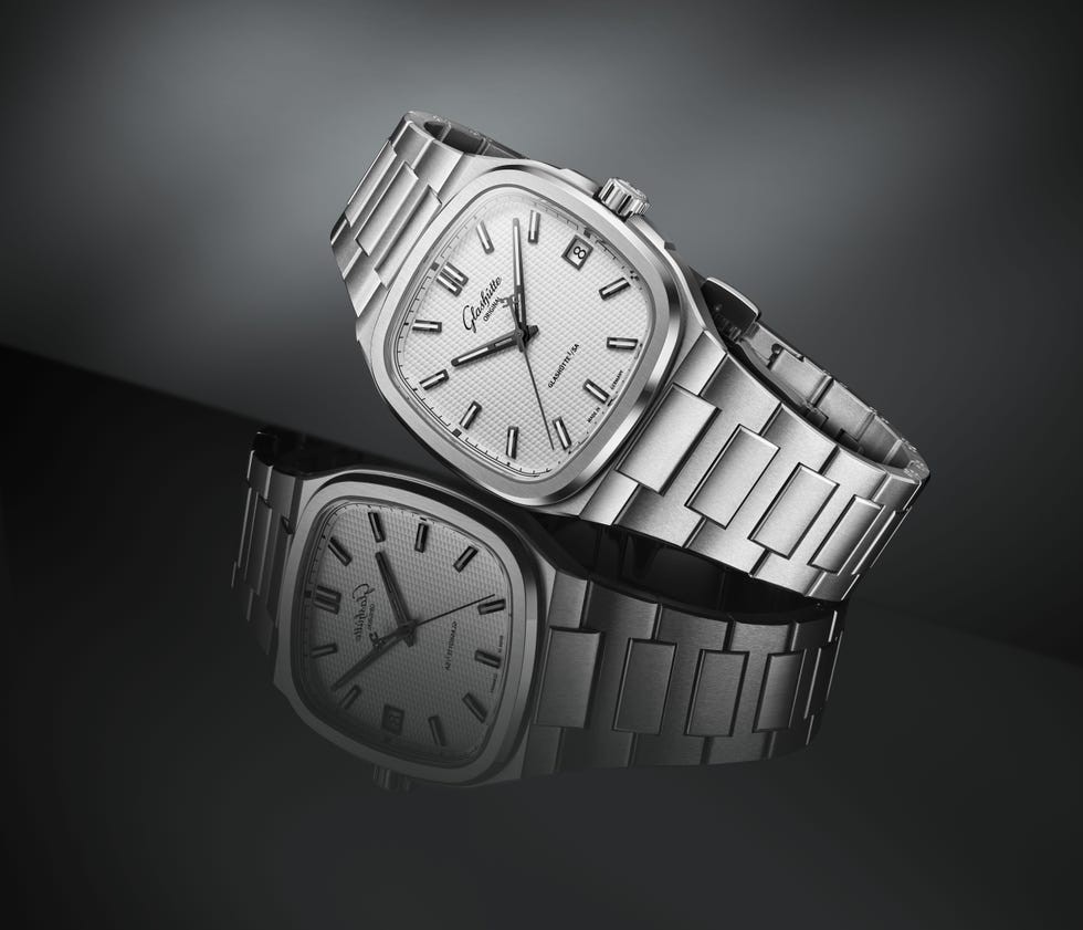 Silver watch with a square face and link bracelet, reflecting on a dark surface.