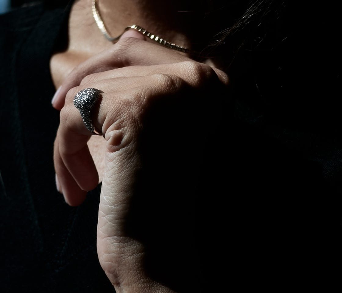 Close-up of a hand adorned with a textured ring, partially illuminated against a dark background.