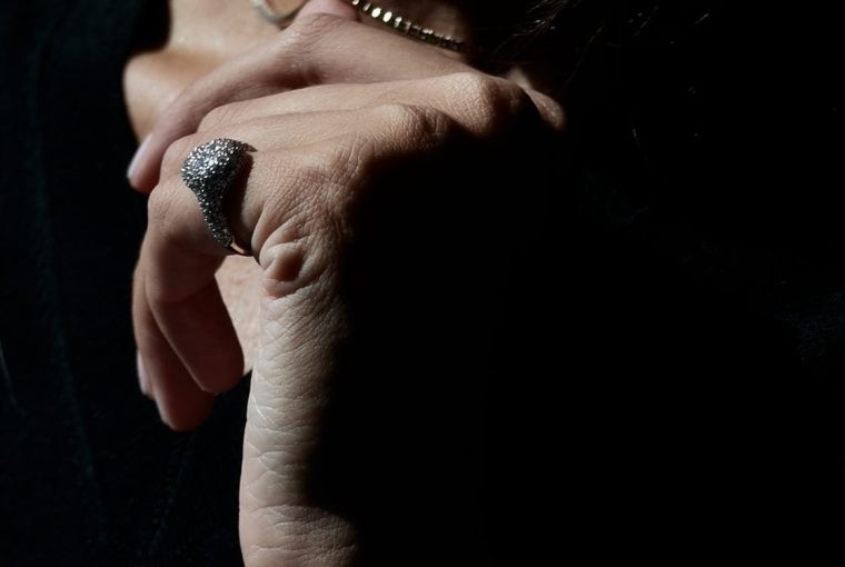 Close-up of a hand adorned with a textured ring, partially illuminated against a dark background.