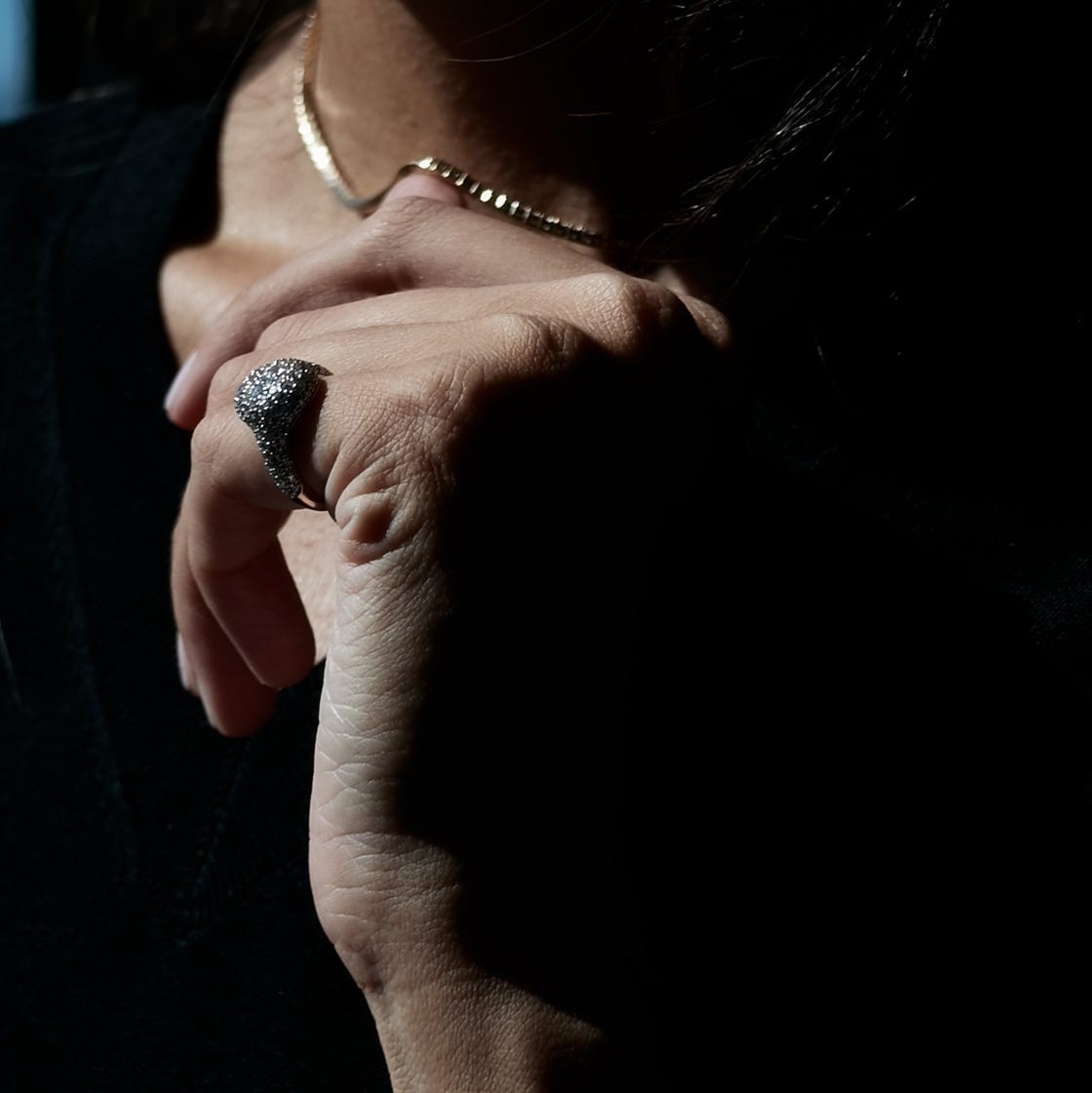 Close-up of a hand adorned with a textured ring, partially illuminated against a dark background.