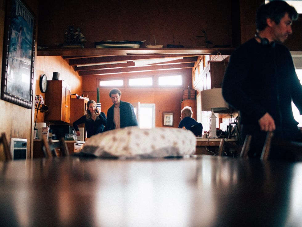 A group of people interacting in a cozy kitchen setting with wooden decor and warm lighting.