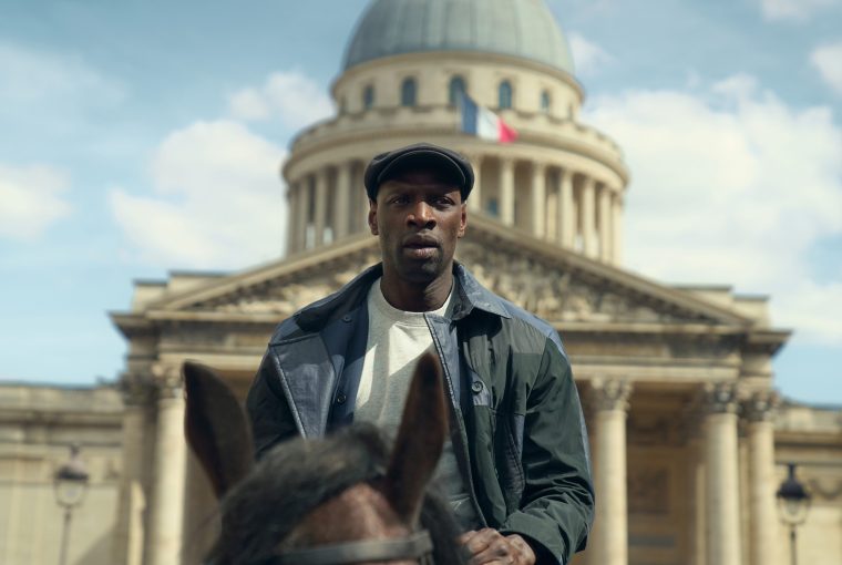 A man on a horse in front of a historic building with a dome and French flags in a clear sky.