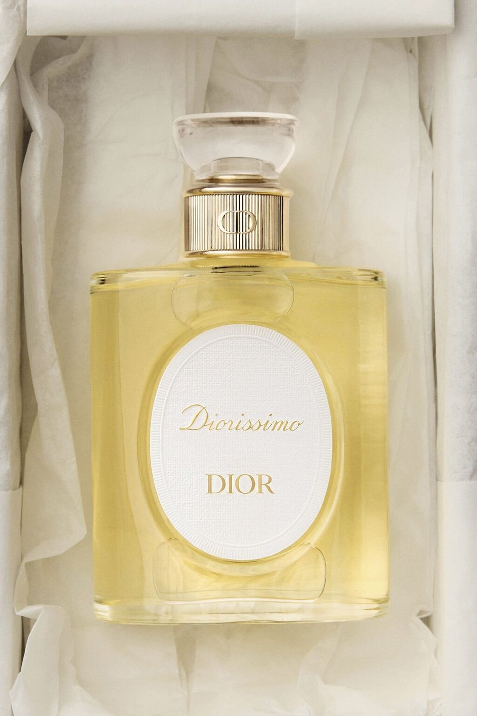 Diorissimo perfume bottle with a gold and white design, displayed in tissue paper packaging.