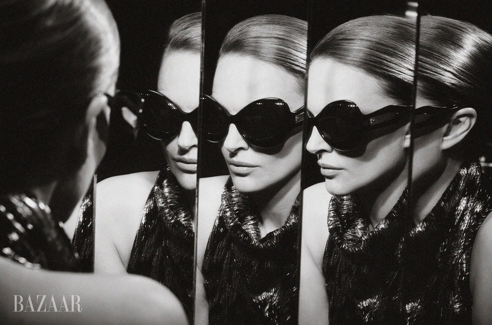 A woman in oversized sunglasses reflected in multiple mirrors, showcasing a glamorous black and white aesthetic.
