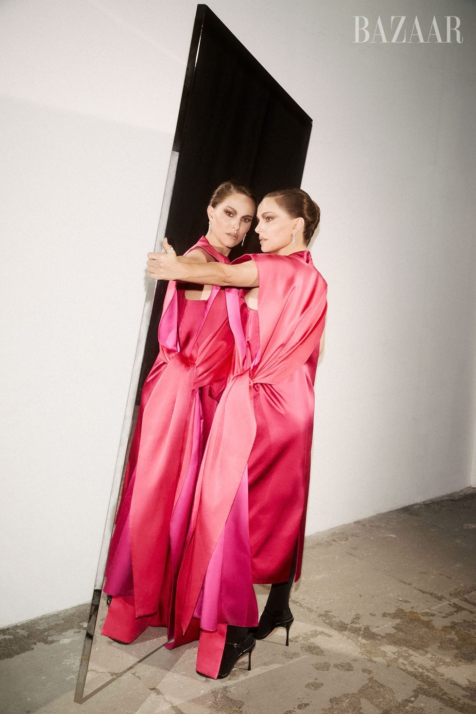 A model in a pink gown poses with a mirror, reflecting her image in an artistic fashion shoot.