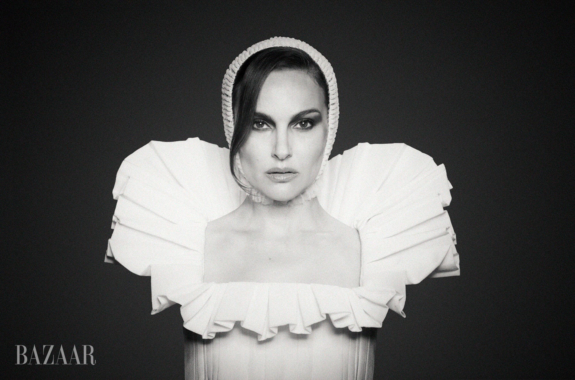 Black and white portrait of a woman in a striking white outfit with dramatic ruffled shoulders and a bonnet.