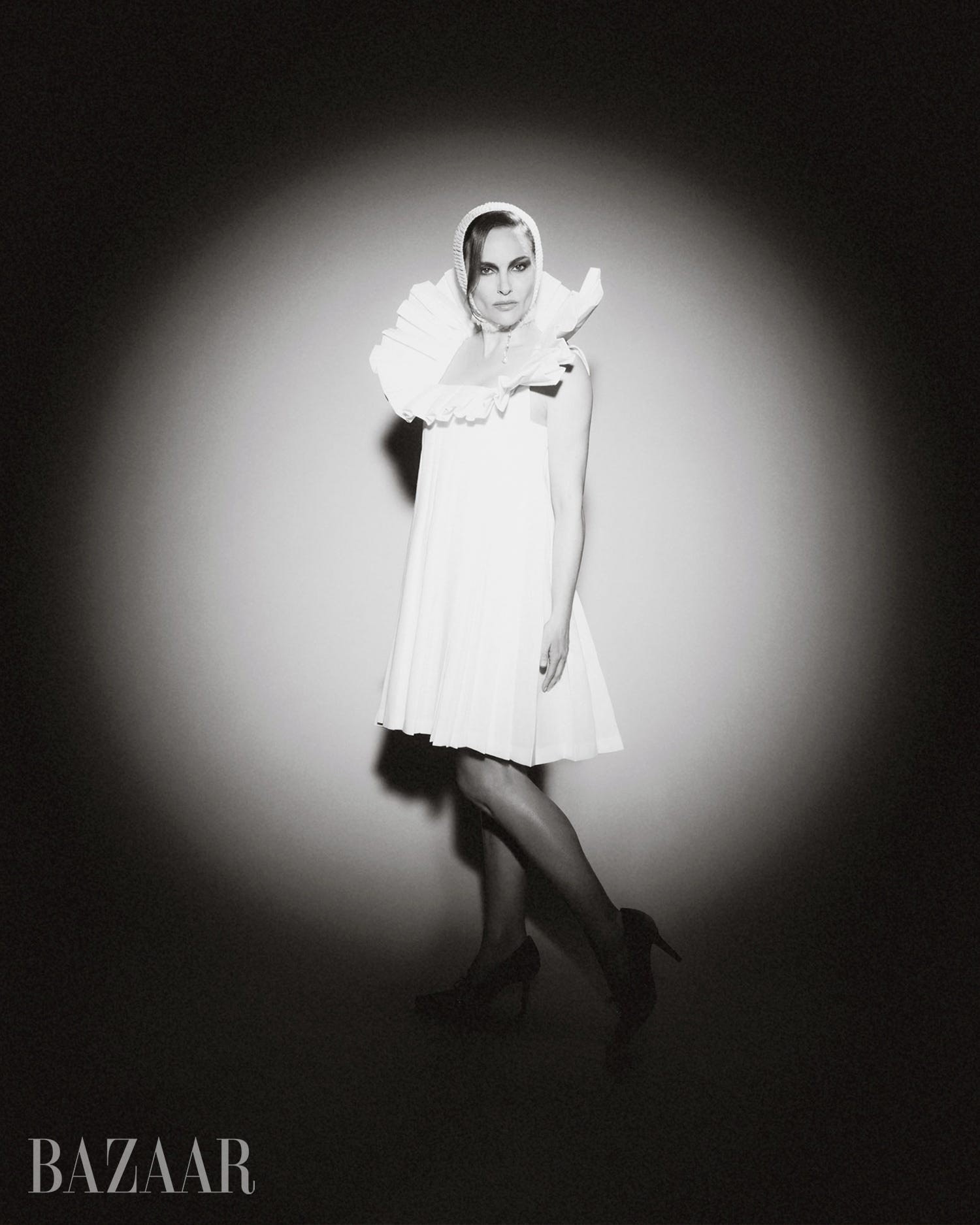A woman in a white dress and ruffled collar poses dramatically in black and white lighting.
