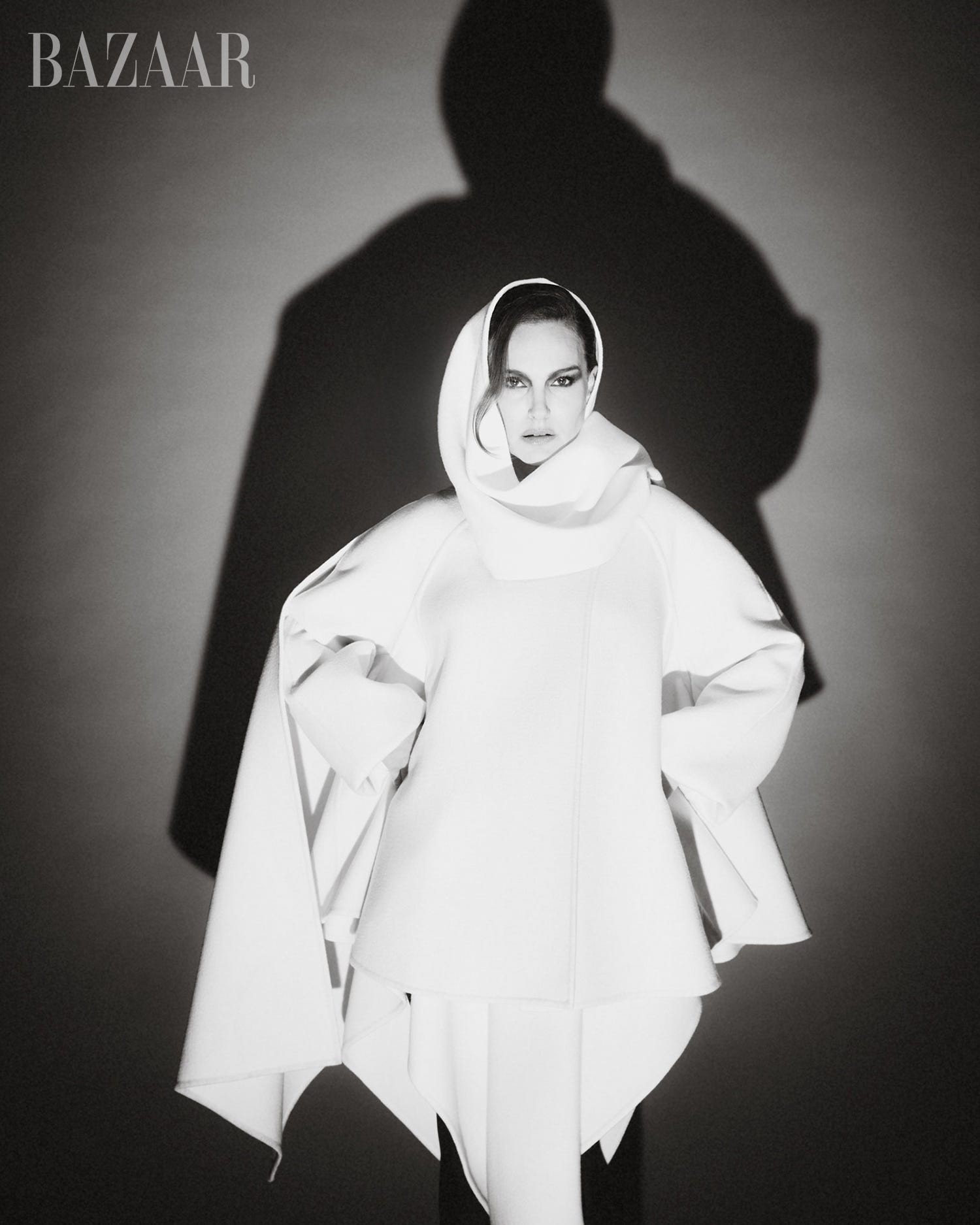 Model posing in a dramatic white outfit with a hood, casting an intriguing shadow against a dark backdrop.