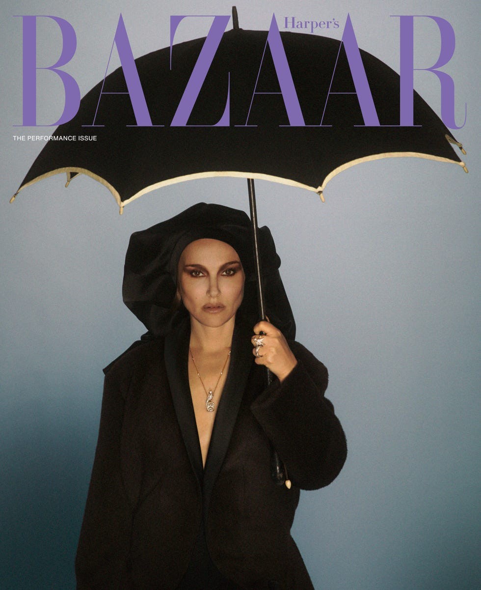 A model in a black outfit holds a black umbrella against a gradient blue background, featured on Harper's Bazaar magazine.