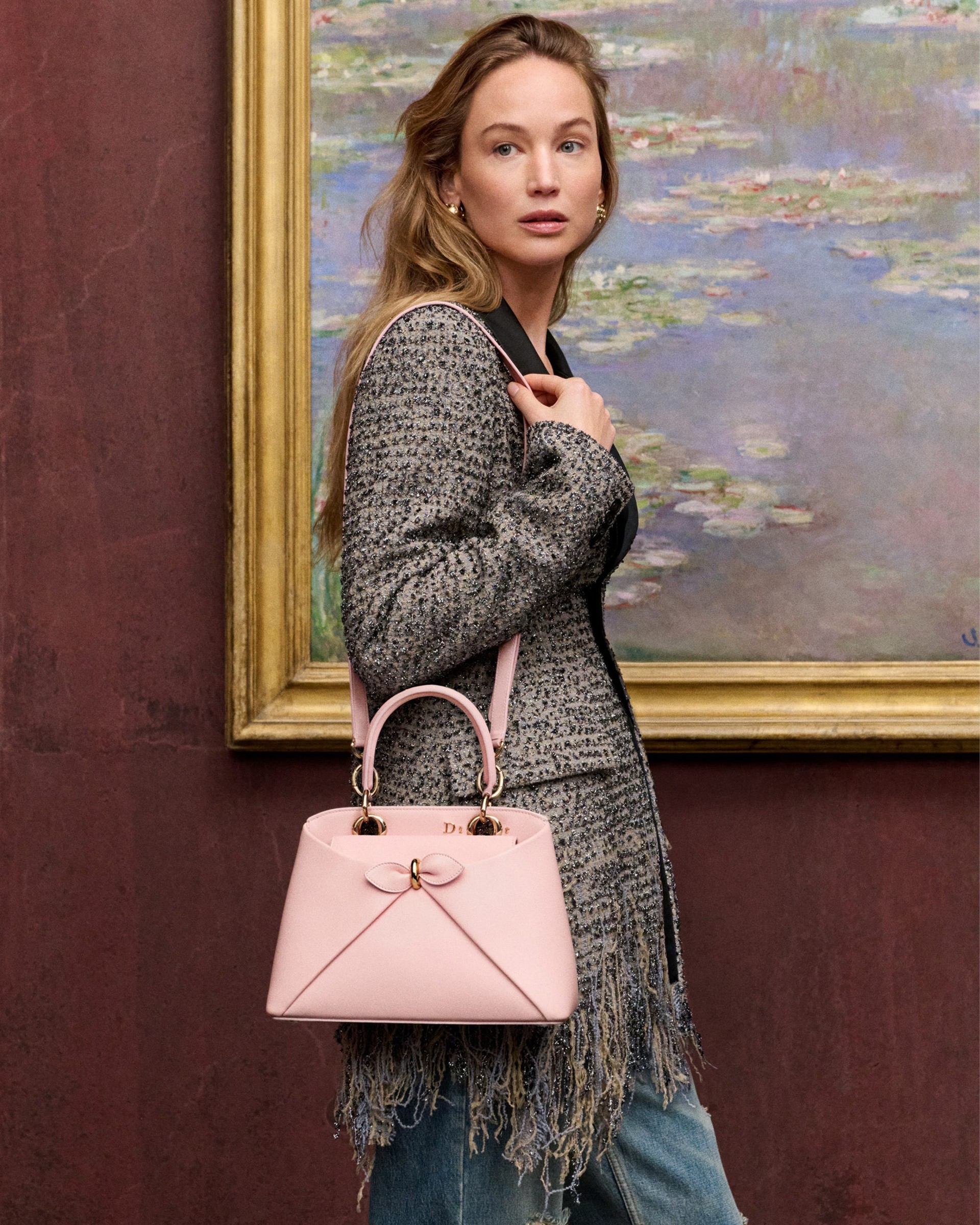 person holding a pink handbag in front of a painting.