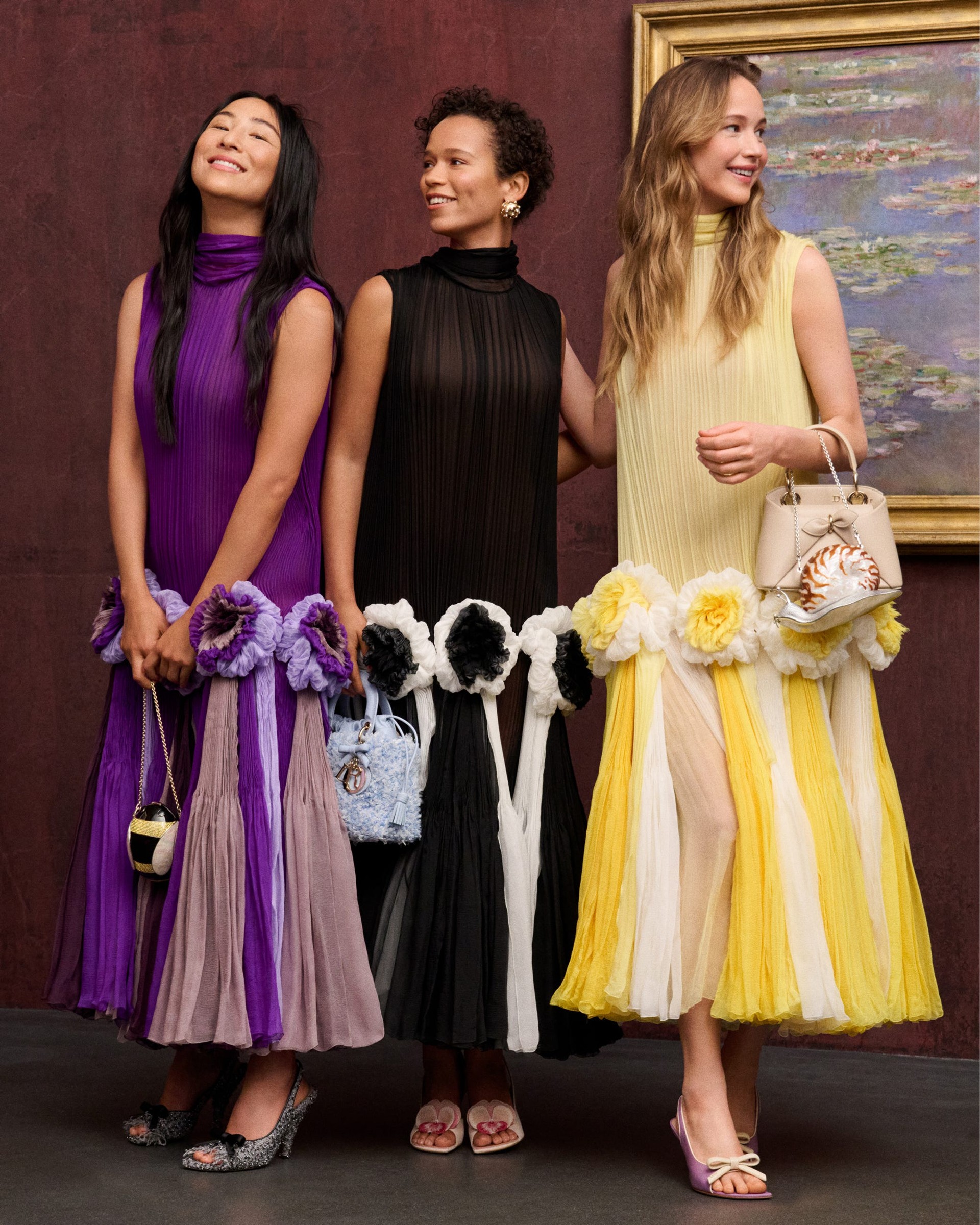 three women in colorful dresses with floral designs, holding small handbags.