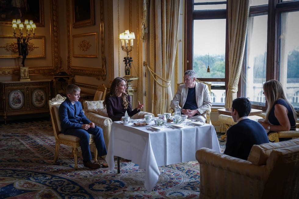 A group having tea and conversation in an elegantly decorated room with large windows.