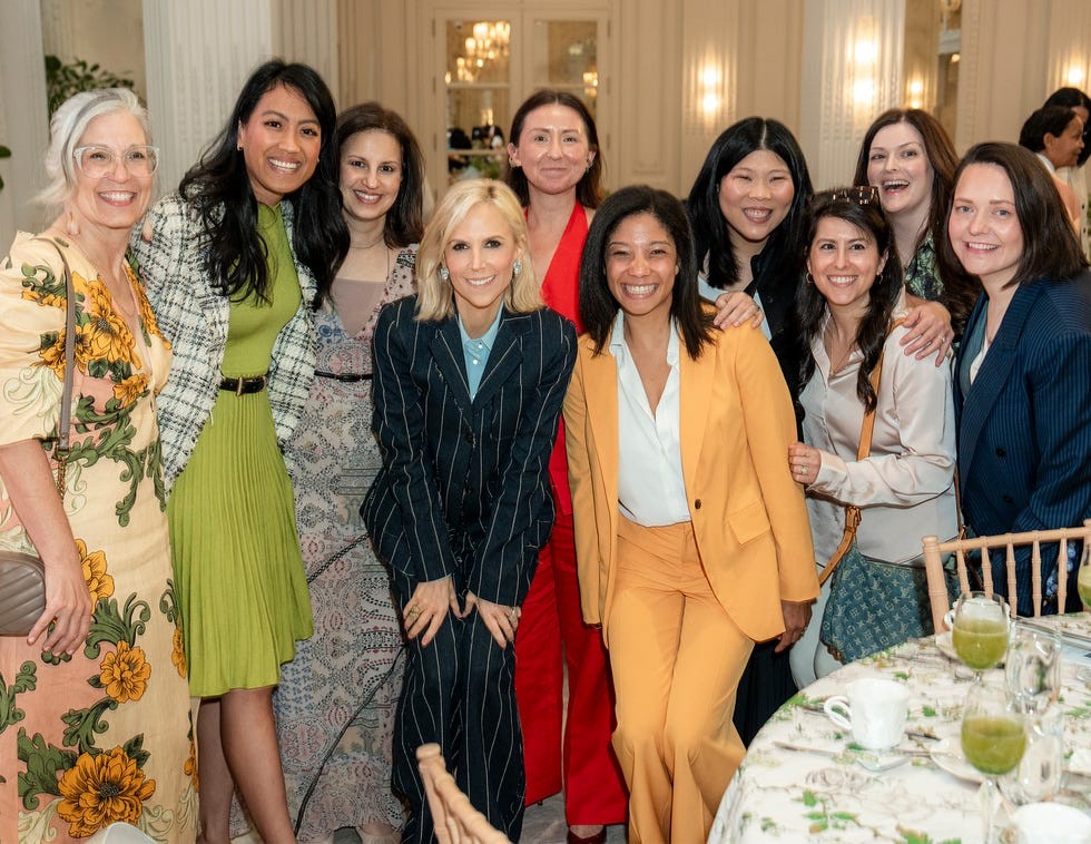 A group of diverse women posing together, smiling at a social event with a beautifully set table in the background.
