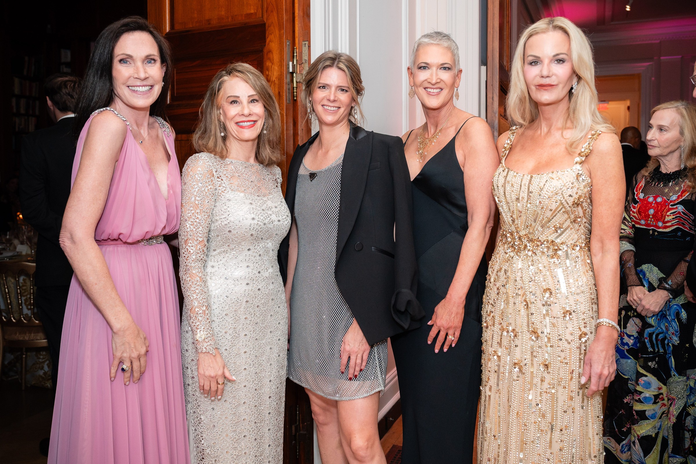 A group of five women in elegant evening attire posing together at a social event.