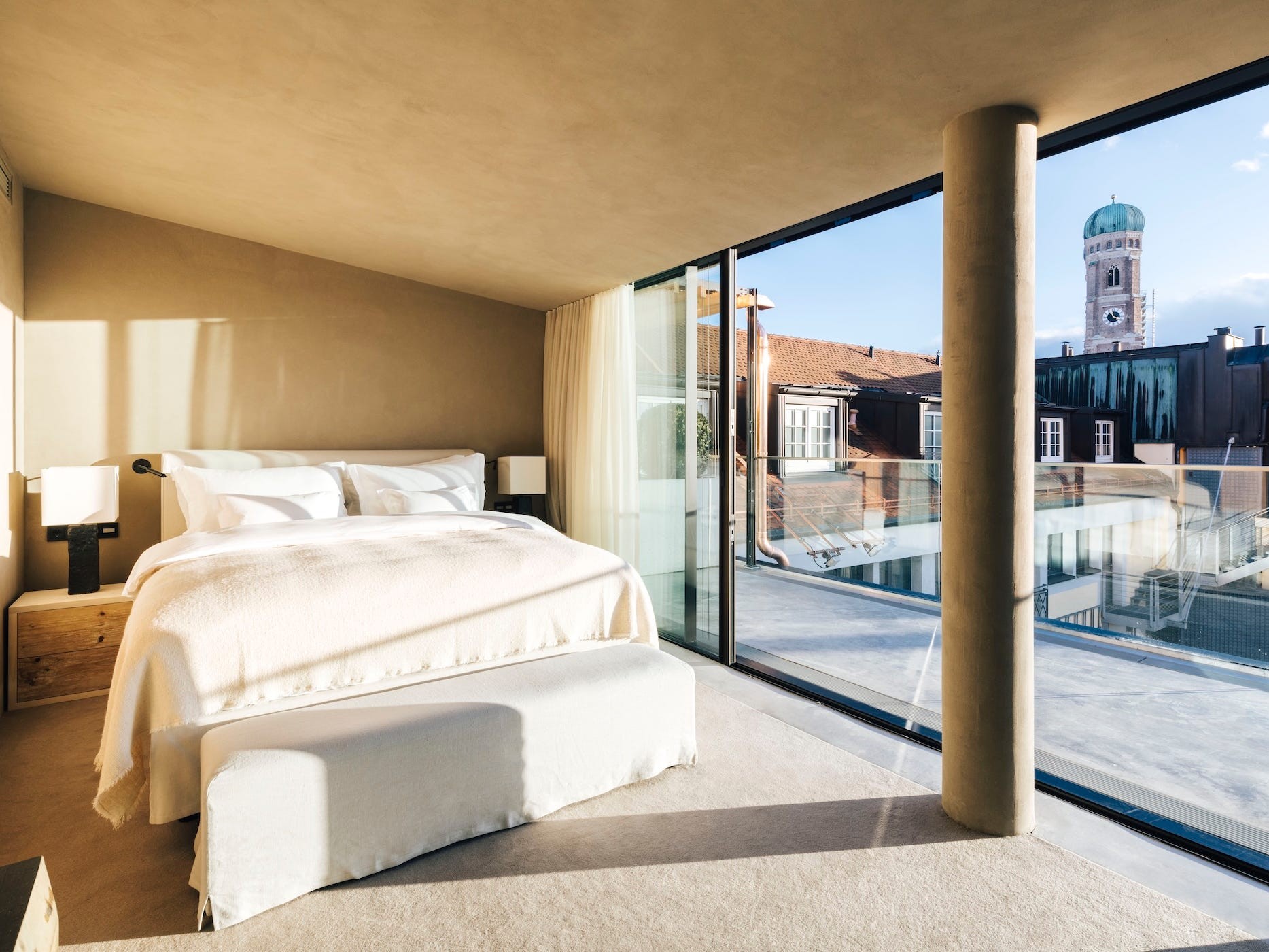 Modern bedroom with a large window showcasing city views and natural light, featuring a cozy bed and minimalist decor.