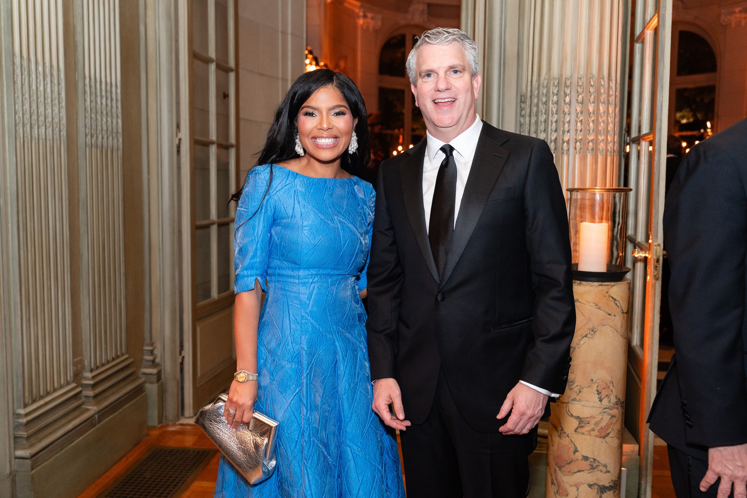 A smiling couple poses together in elegant attire at a formal event.