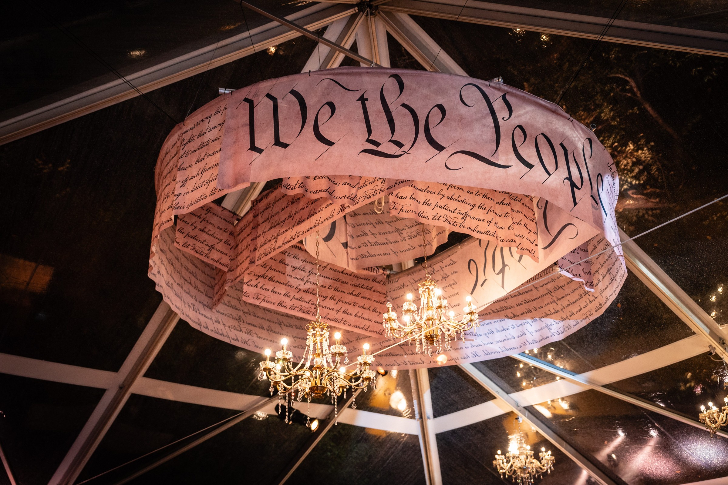 Decorative banner with "We the People" text hanging from a canopy, featuring chandeliers below.