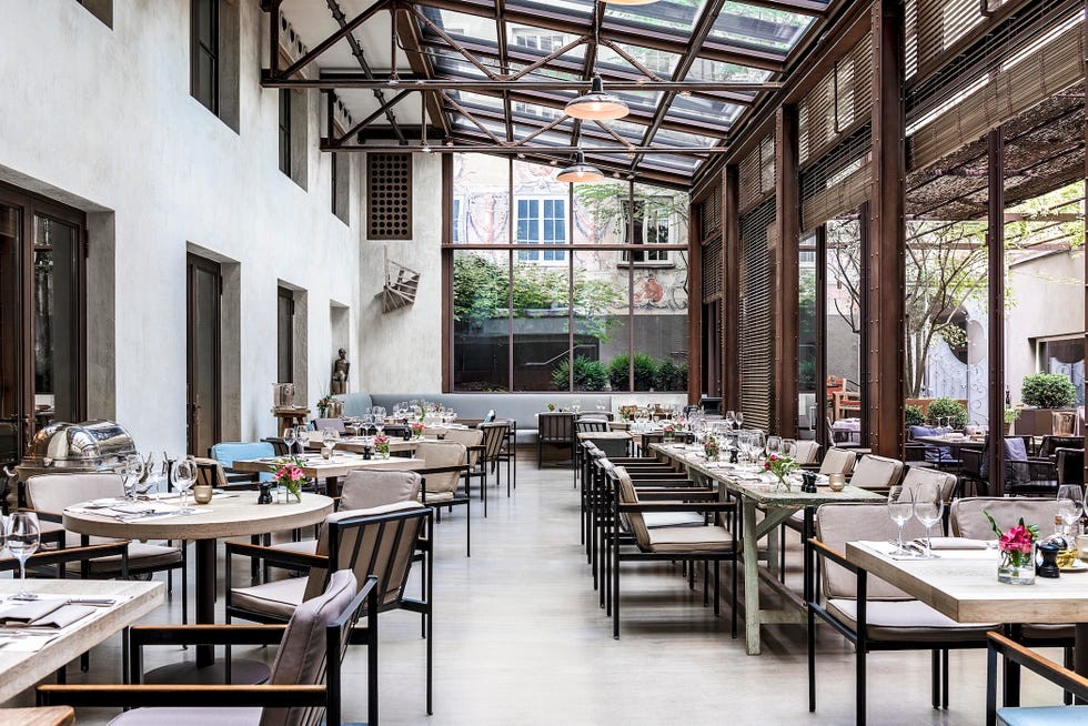 Modern restaurant interior with glass ceiling, wooden accents, and elegantly set tables with floral centerpieces.