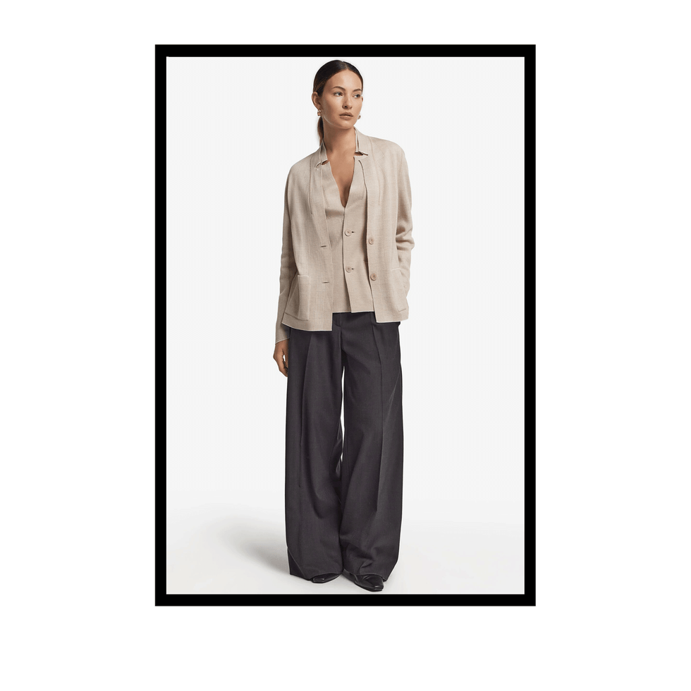 Model wearing a beige blazer over a top and wide-leg black pants with a minimalist background.