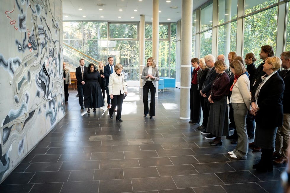 A group of people walking through a modern building with a mural on the wall and large windows.