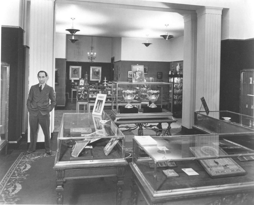 A man standing near display cases in a museum featuring various artifacts and artworks.