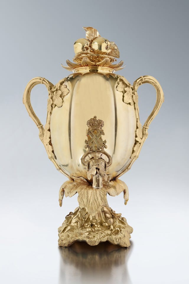 Ornate golden trophy with a decorative lid, featuring fruit and leaf motifs, on an intricately designed base.