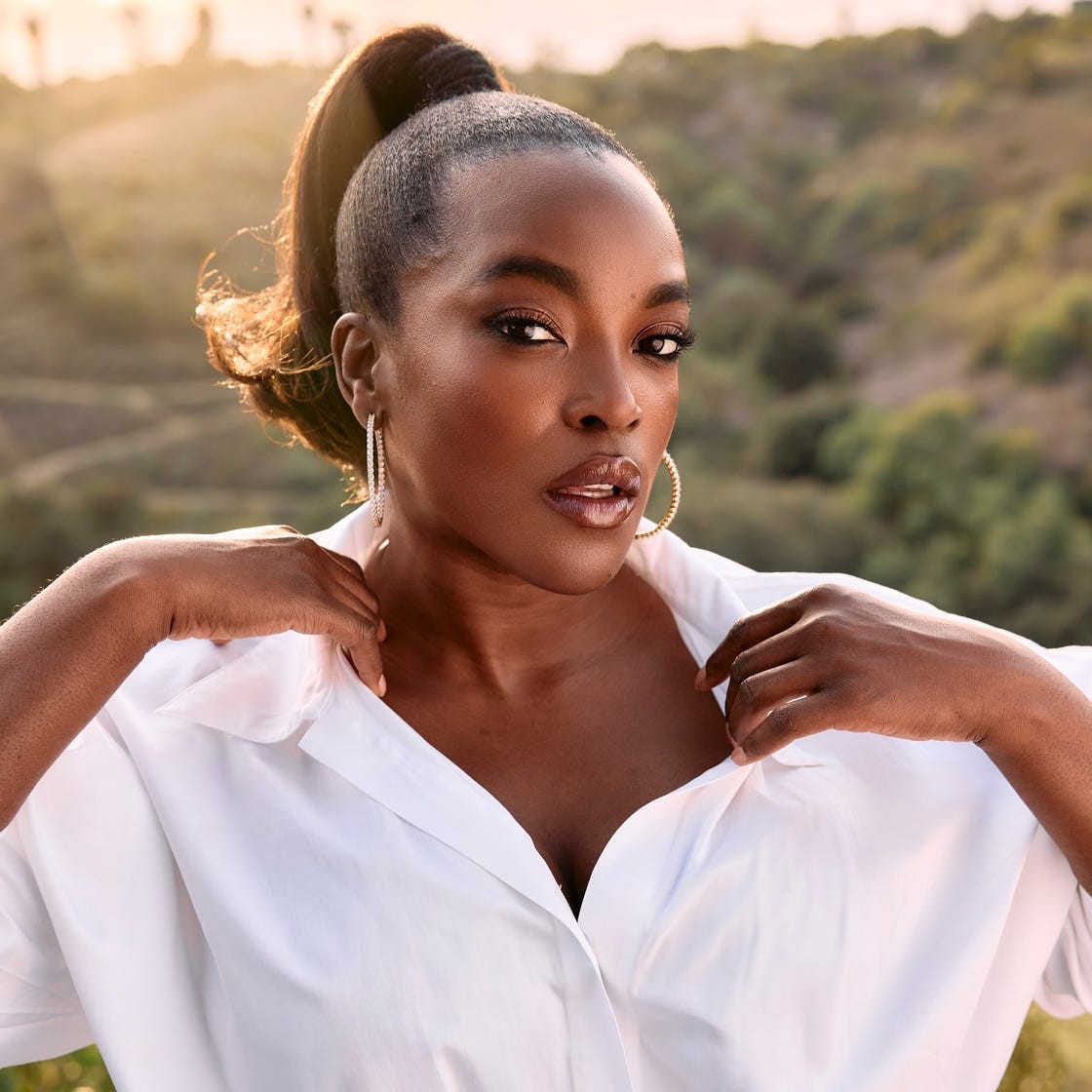 Woman in a white shirt with denim jeans poses confidently outdoors against a scenic background during sunset.
